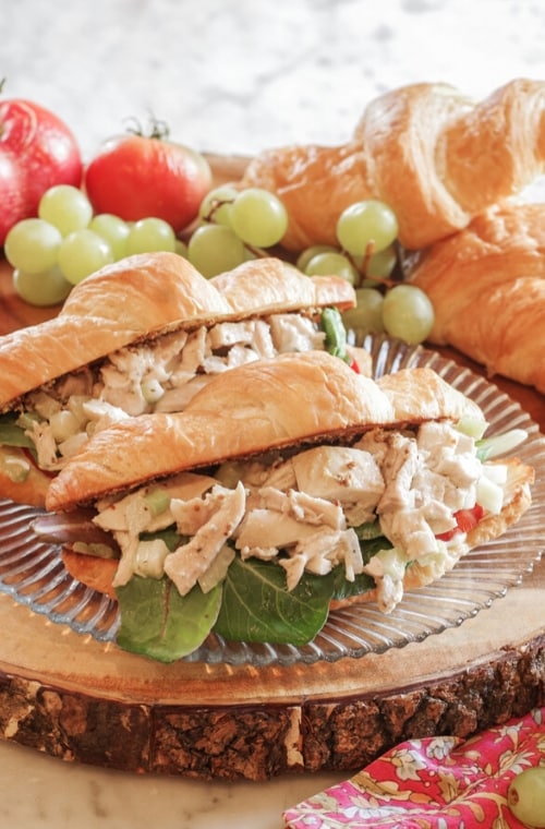 chicken salad sandwich on croissant on a wood board with grapes behind the sandwich