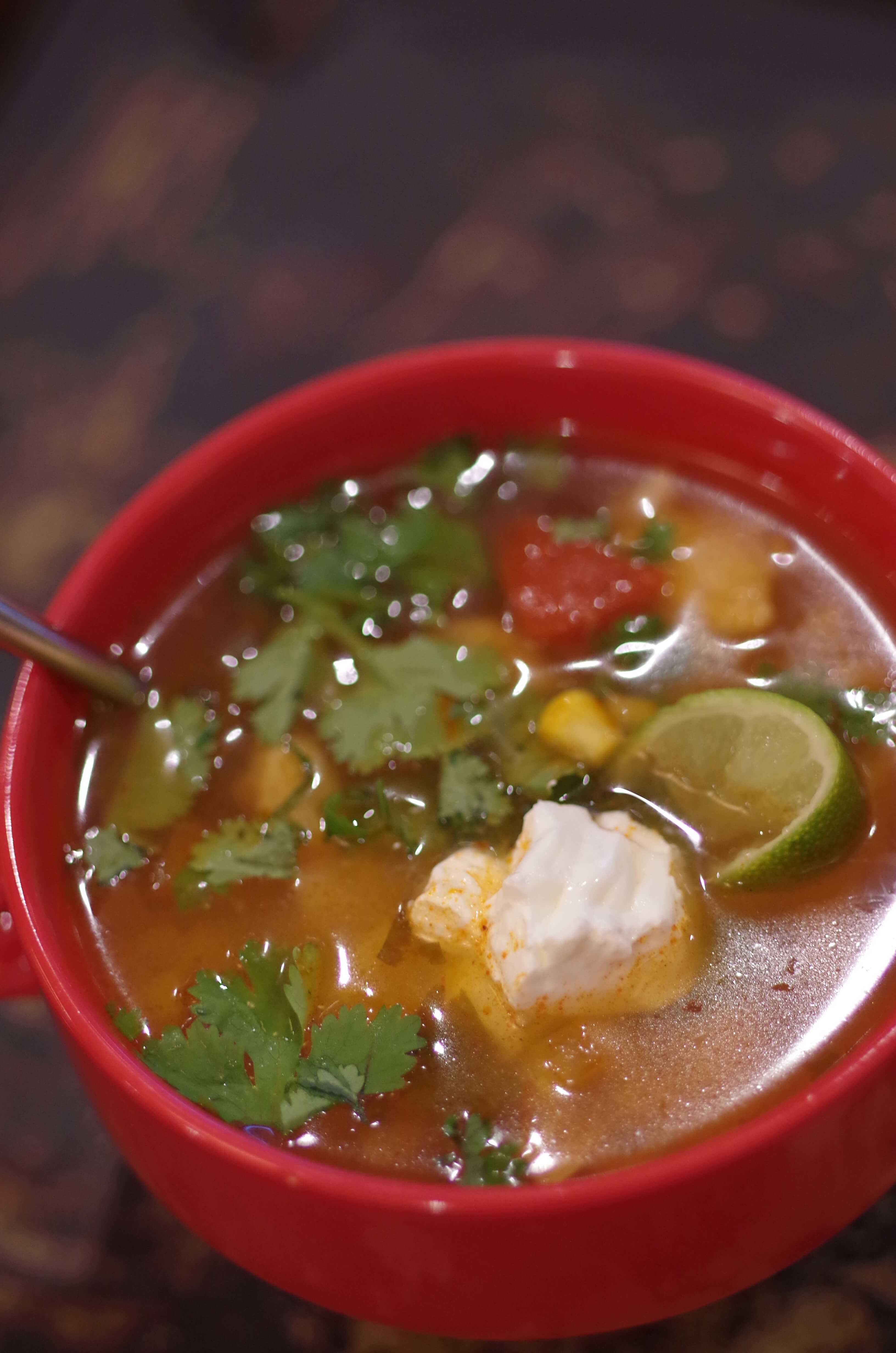 chicken tortilla soup in a red mug with a handle, garnished with sour cream, lime, and cilantro.