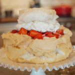 Strawberry Schaum Torte with whip cream and strawberries on a white pedestal cake plate