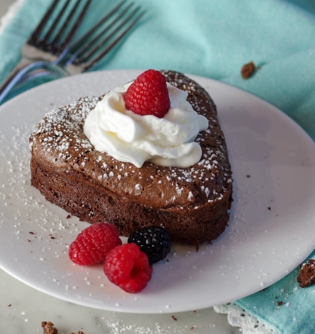 heart shaped chocolate cake with whip cream and raspberries