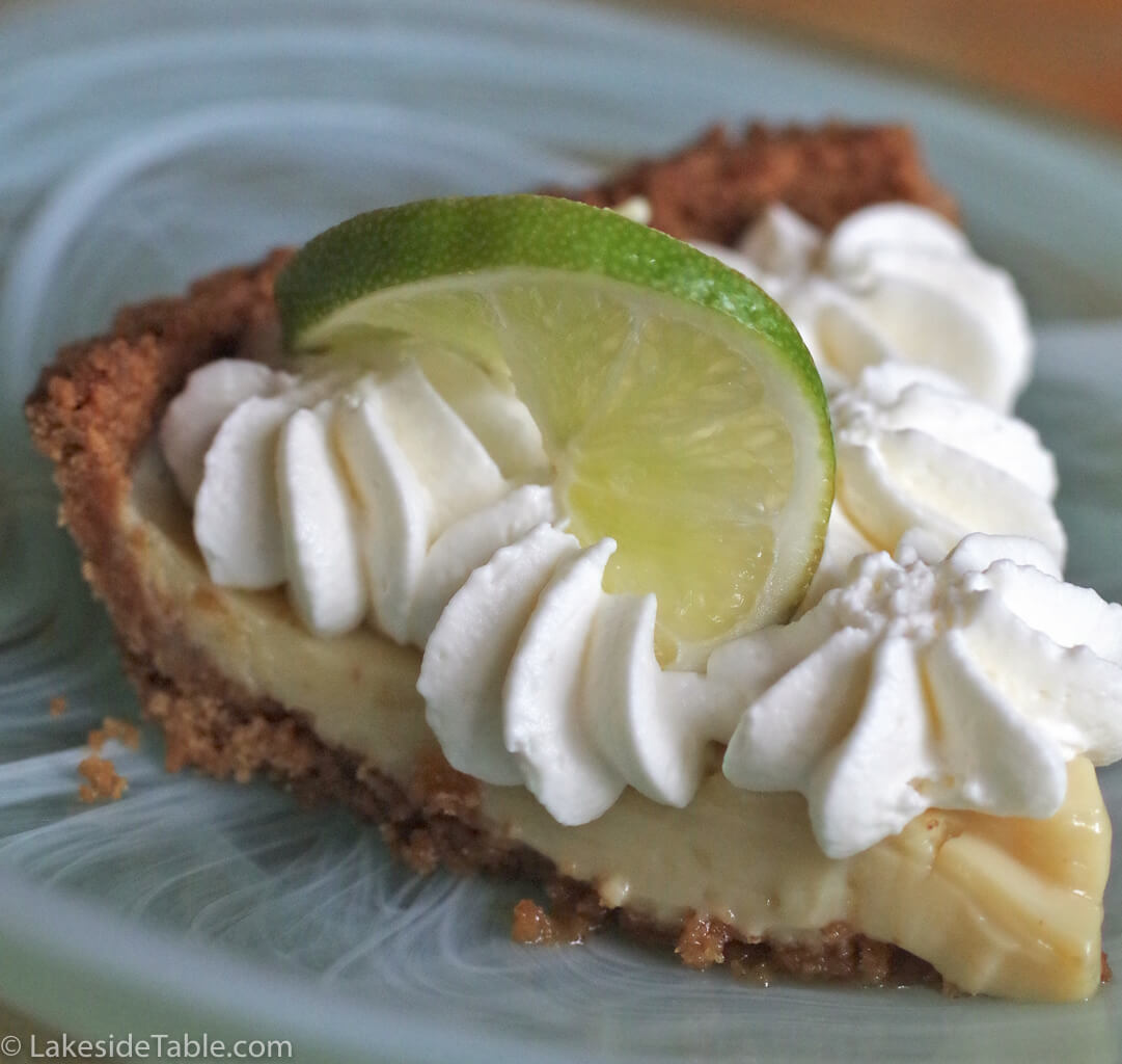 close up picture of a slice of key lime pie with graham crust, whip cream and lime