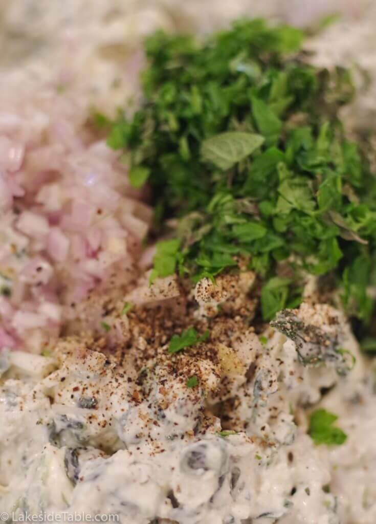 close up of fresh chopped herbs, minced onion and cream cheese. ready to be mixed up for spinach artichoke dip recipe