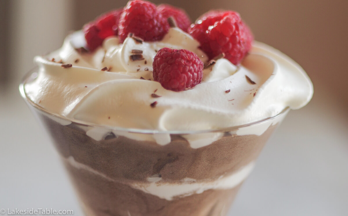 layered chocolate mousse with whip cream topped with raspberries and chocolate shavings