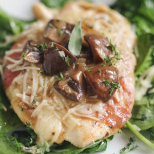 Chicken wrapped in prosciutto covered in mushrooms and cheese over spinach