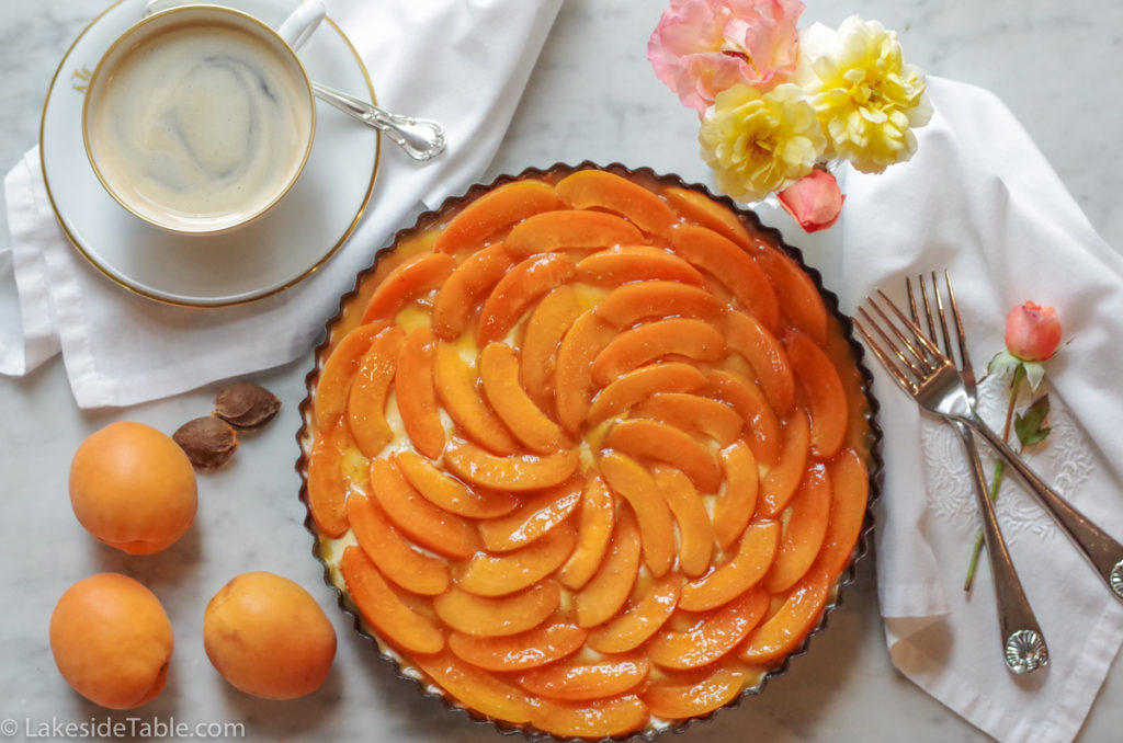 apricot tart next to a cup of coffee and peach and yellow roses in a crystal vase