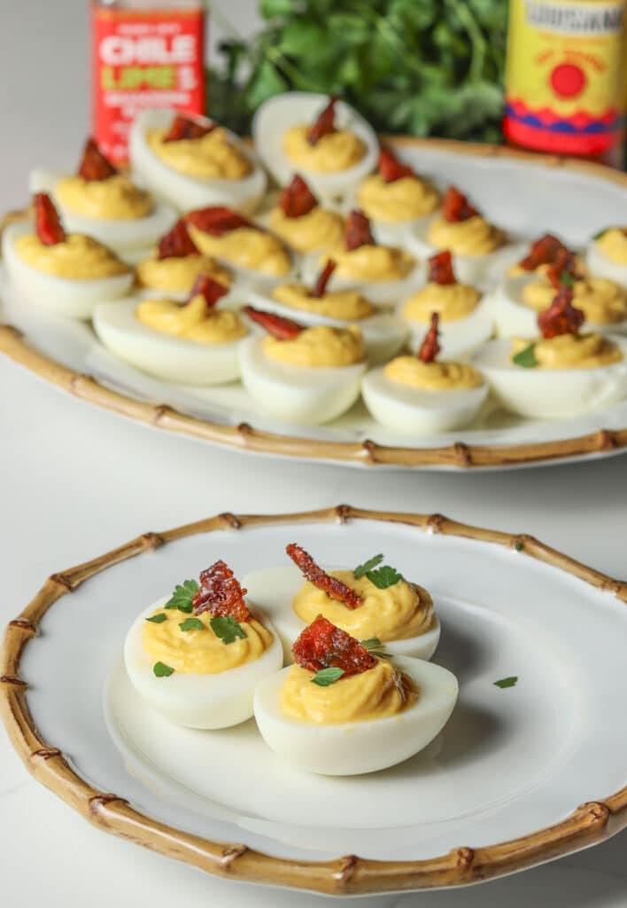 deviled eggs on white bamboo plate with tray of deviled eggs behind