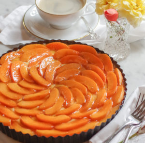 apricot tart next to a cup of coffee and peach and yellow roses in a crystal vase