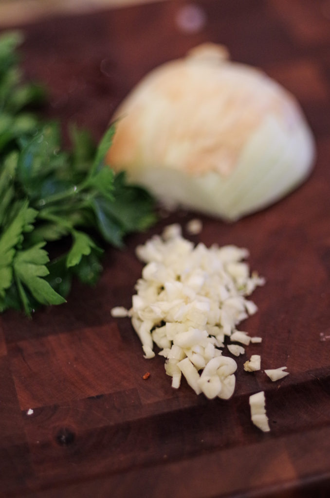 chopped up garlic, onion and parsley on chopping block