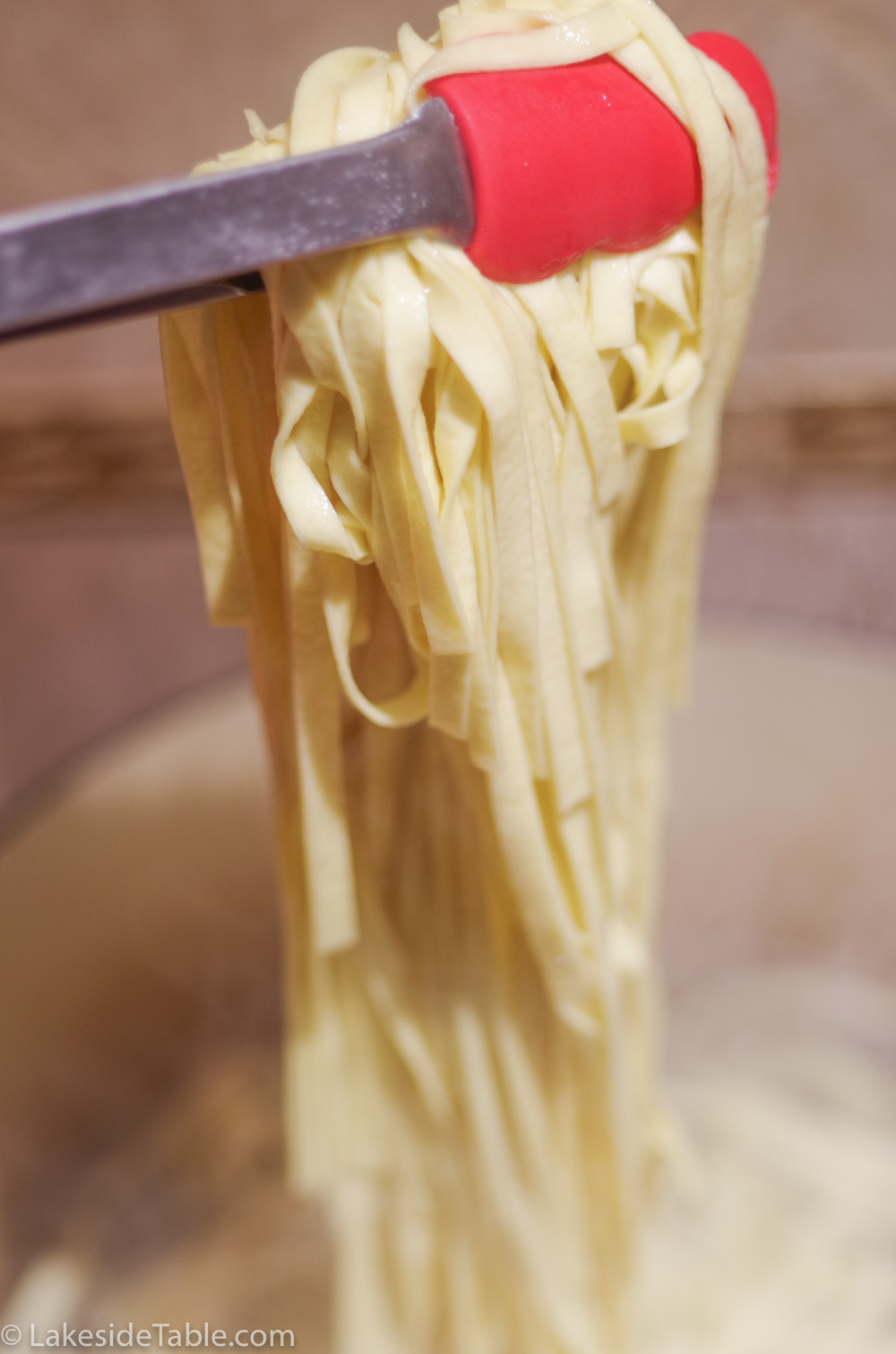 pulling fresh pasta out of the water with red tongs