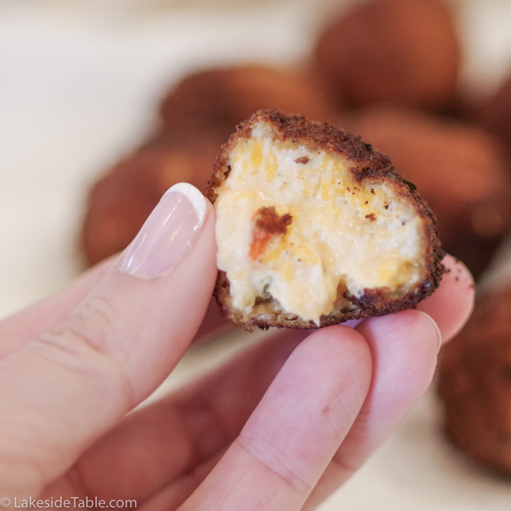 close up shot of a hand holding a creamy cheesy fried pimento cheese ball with a bite taken out of it