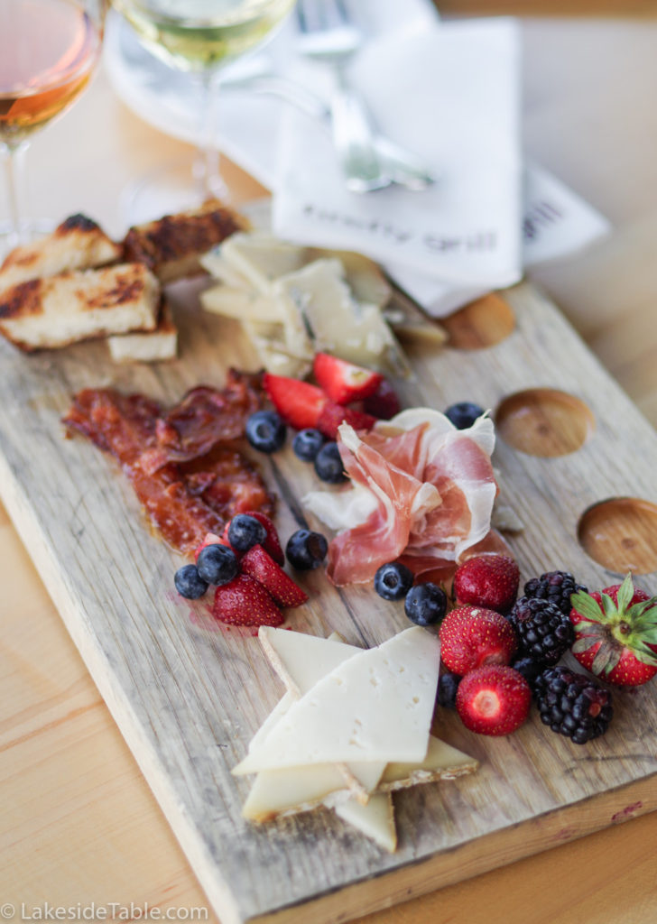 Charcuterie board of blue cheese, swiss cheese, fruit, bacon, and ham on a Firefly Grill wooden board