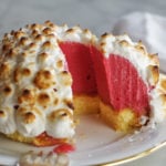 close up of an ice cream bombe dessert with raspberry red ice cream, yellow pound cake and toasted meringue on top