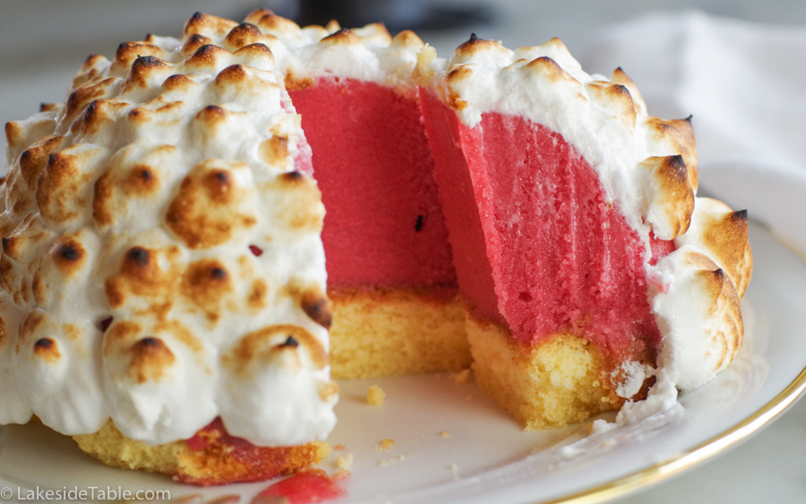 close up of an ice cream bombe dessert with raspberry red ice cream, yellow pound cake and toasted meringue on top