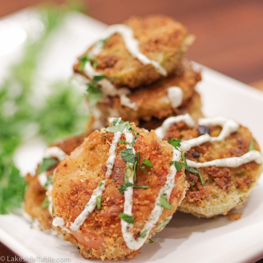 A stack of fried green tomatoes golden brown and crispy with herb mayo on a white plate