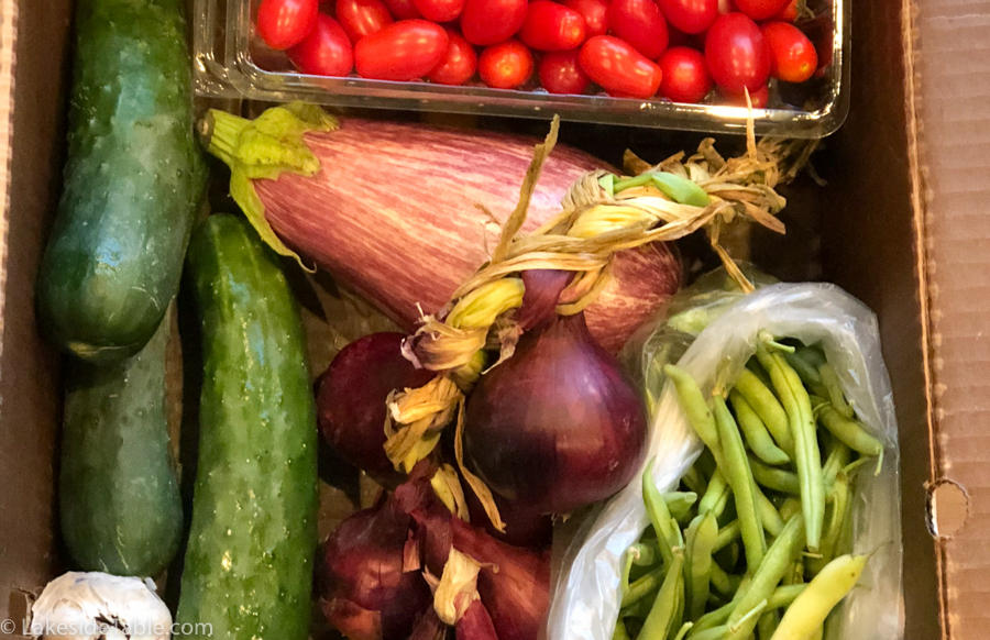 Box full of organic produce: cherry tomatoes, cucumbers, eggplant, garlic, beans and onions