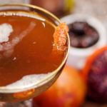 Close up of blood and sand cocktail in a coup glass with orange peel garnish