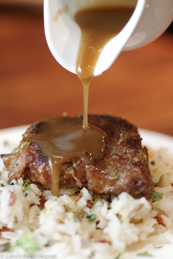 sauce pouring over steak on wild rice from a white pitcher
