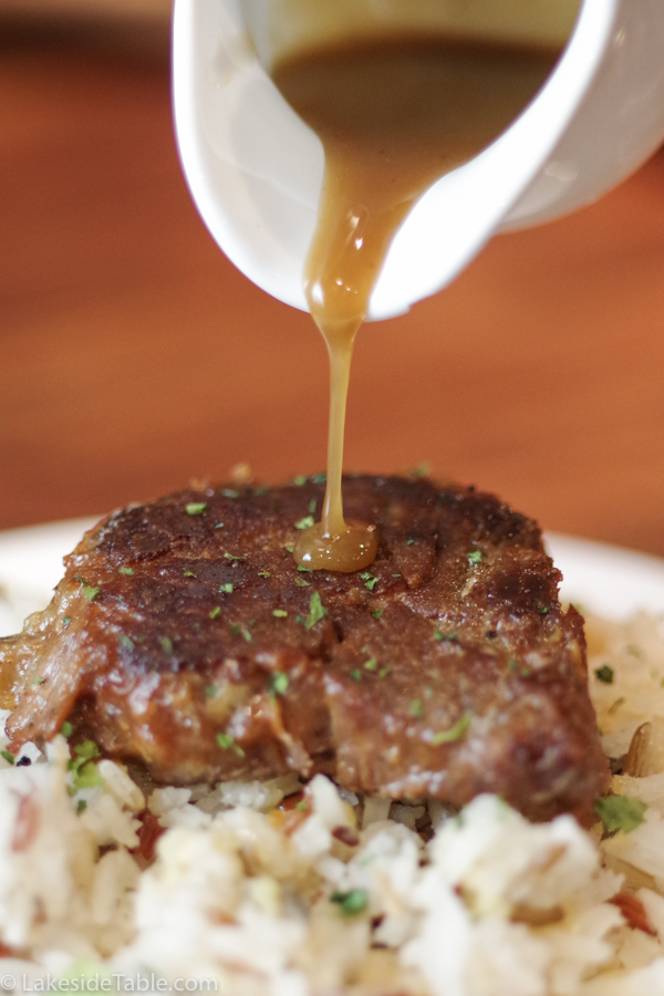 sauce pouring over steak on wild rice from a white pitcher