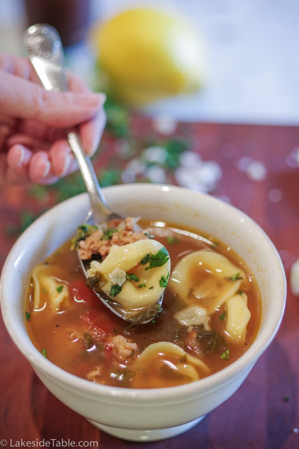 Easy tortellini soup with turkey sausage and parmesan cheese in a white bowl with a spoonful ready to eat