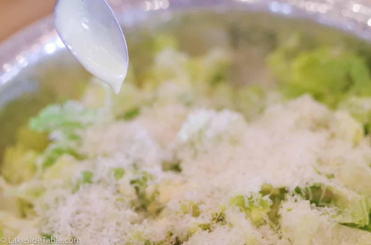 spoon drizzling parmesan dressing over a simple salad
