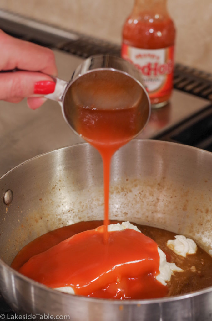 pouring hot sauce over cream cheese in sauce pan