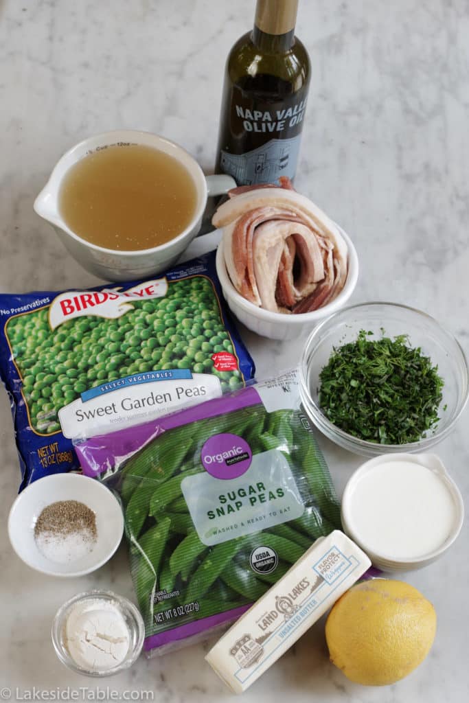 All the ingredients for the recipe laid out: chicken broth, oil, butter, bacon, peas, snap peas, chopped herbs, salt & pepper, cream, lemon and flour
