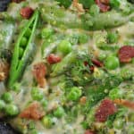 close up of creamy peas with bits of bacon in a black bowl