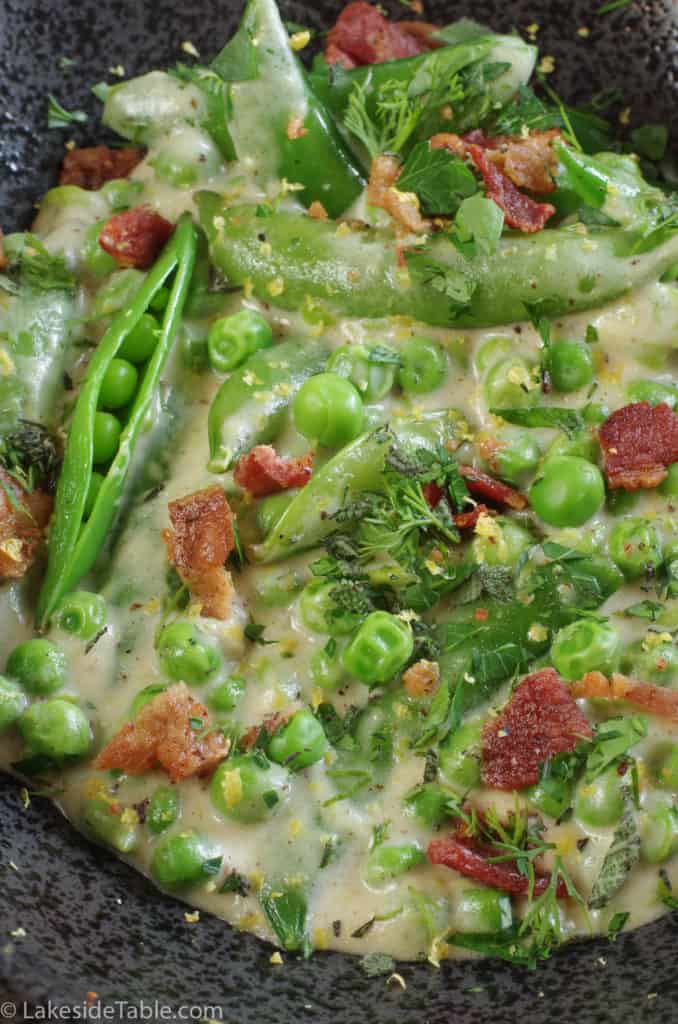 close up of creamy peas with bits of bacon in a black bowl