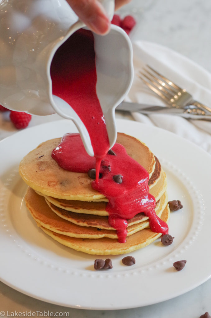 raspberry sauce being poured over chocolate chip pancakes 