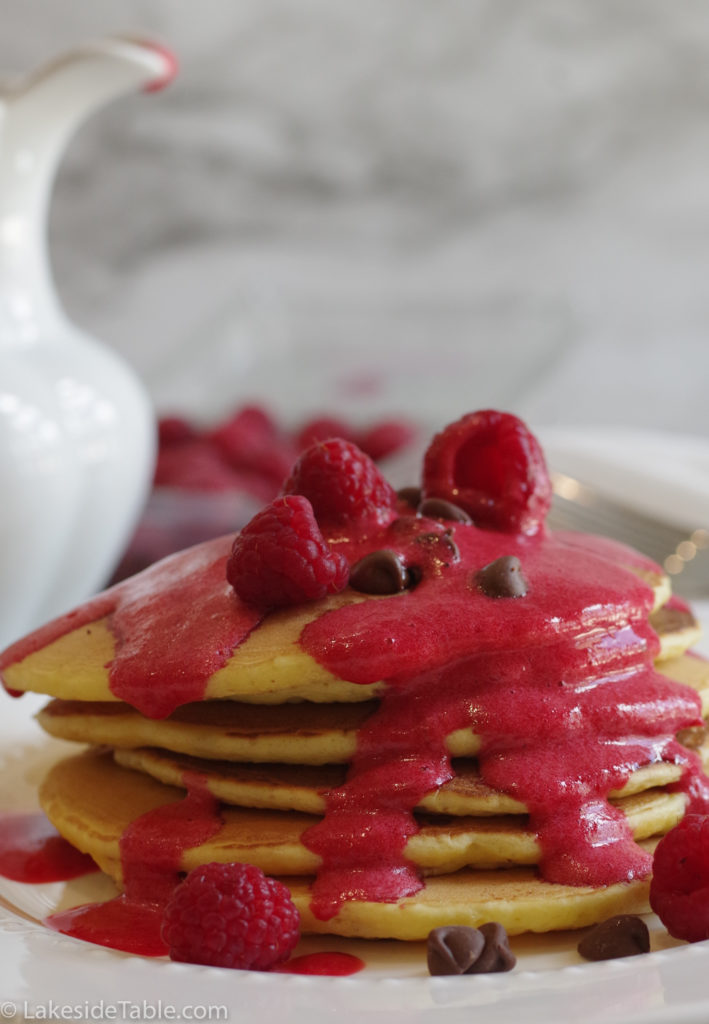 raspberry sauce being poured over chocolate chip pancakes