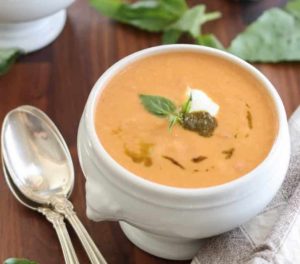 tomato soup with pesto, basil and sour cream in a white bowl