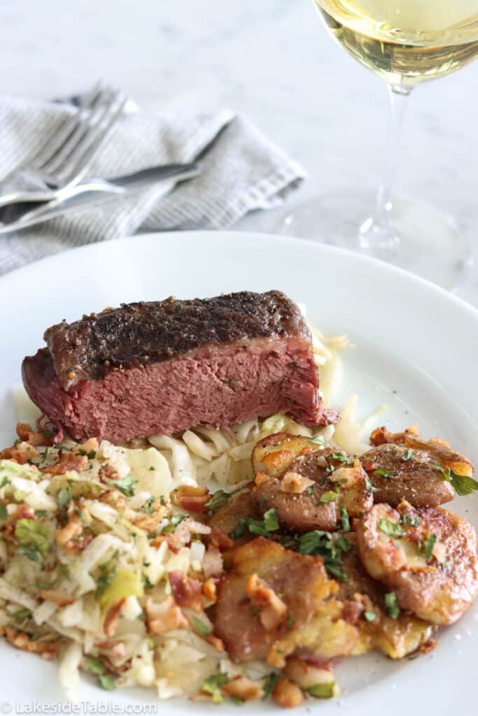 oven baked corned beef on a white plate with sauteed cabbage and smashed potatoes with a glass of white wine
