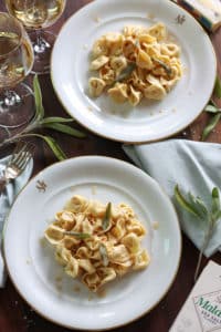 2 plates of finished tortellini pasta dripping with brown butter sauce topped with crispy sage leaves
