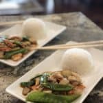 moo goo gai pan on a white plate with a ball of white rice and chop sticks