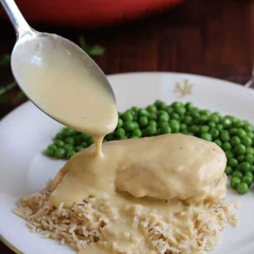 veloute sauce over chicken and rice with peas on a white plate