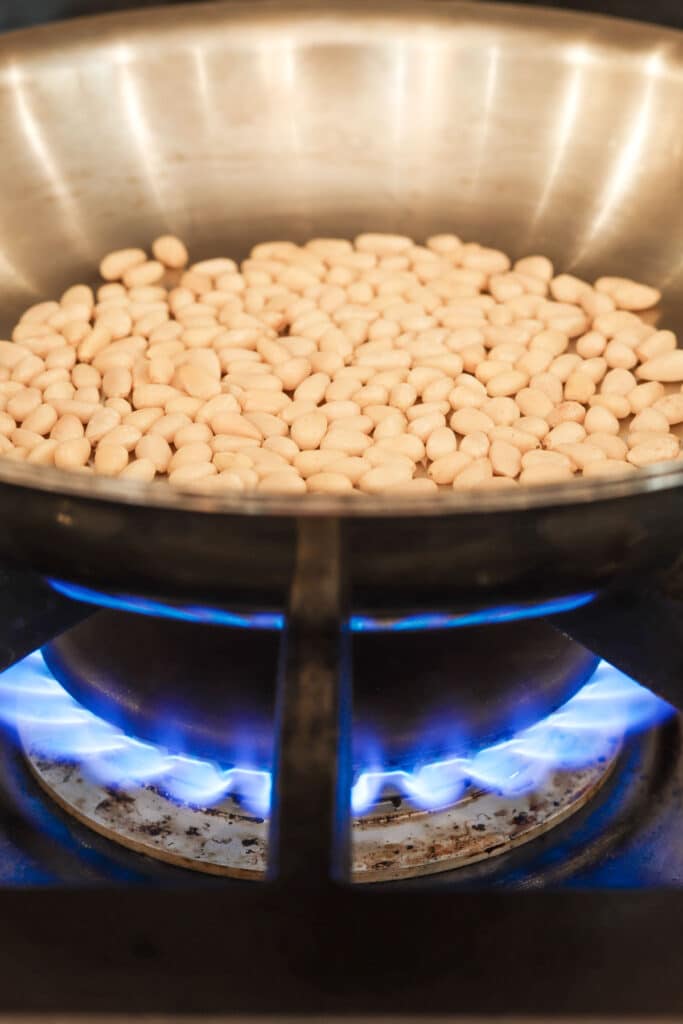 pine nuts toasting in a skillet over blue flame