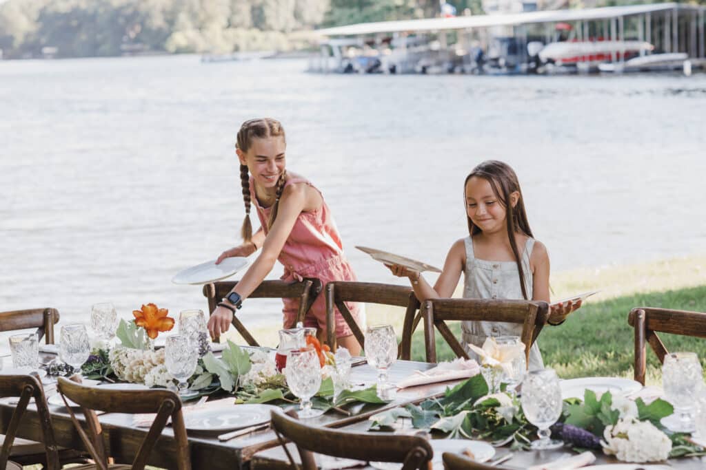 2 girls setting a table with a lake in the background