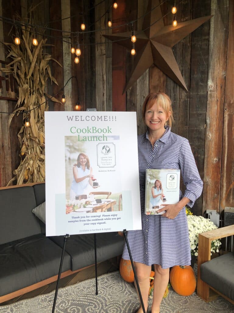 Madalaine holding her cookbook at the firefly restaurant with cookbook launch poster