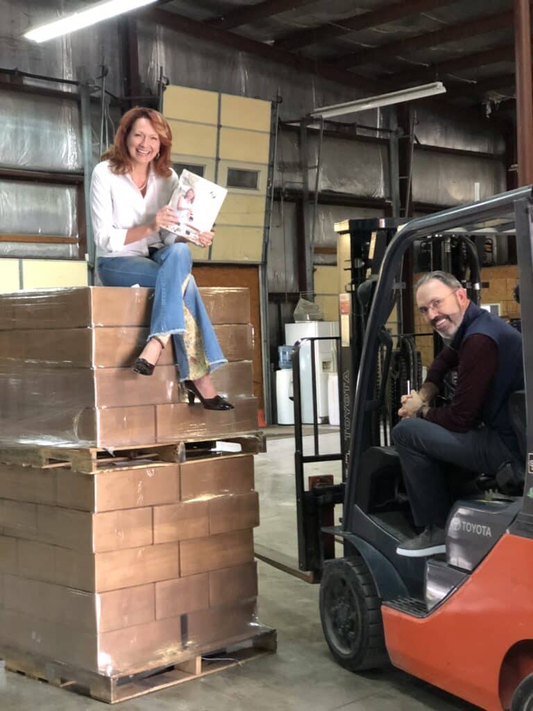 madalaine sitting on 2 pallets of books and jerry in forklift