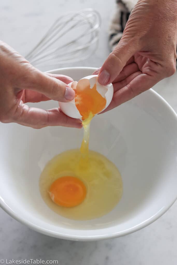 dropping 2 eggs into a white bowl sitting on a white marble table