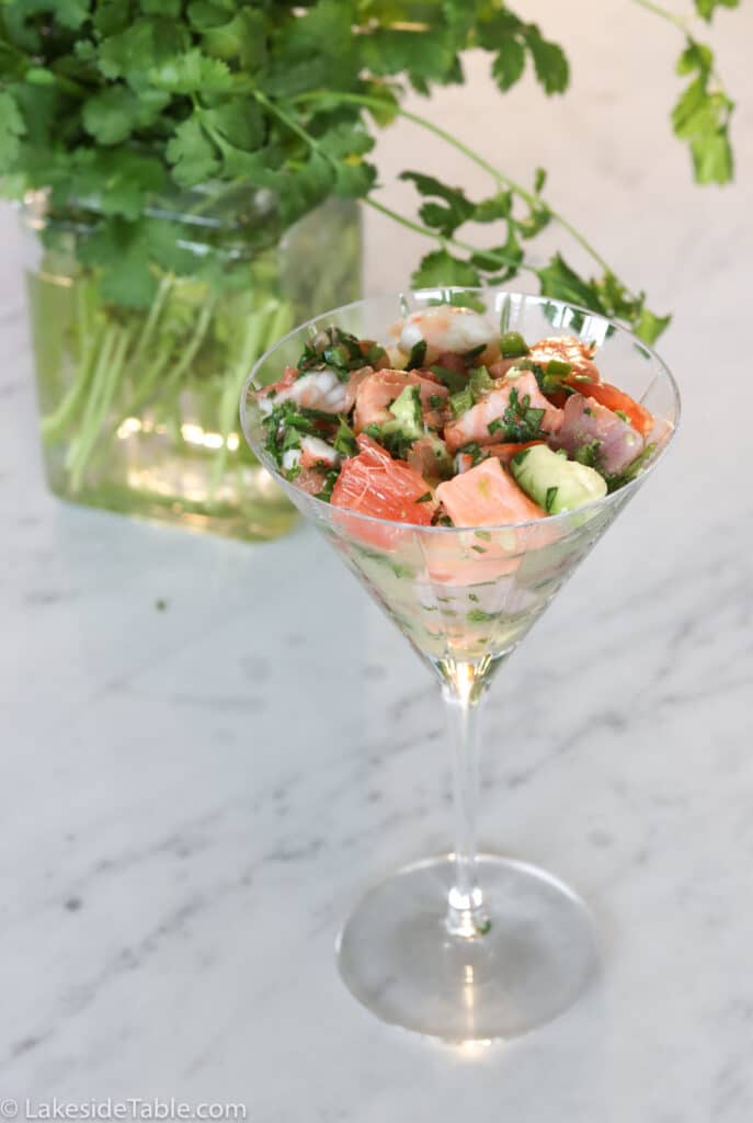 martini glass filled with ceviche appetizer with fresh green cilantro behind it