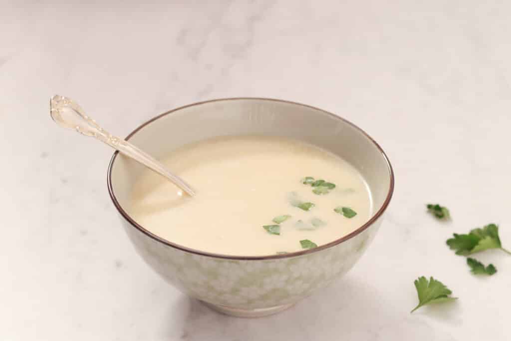 bowl of cauliflower soup topped with parsley on a white marble table top