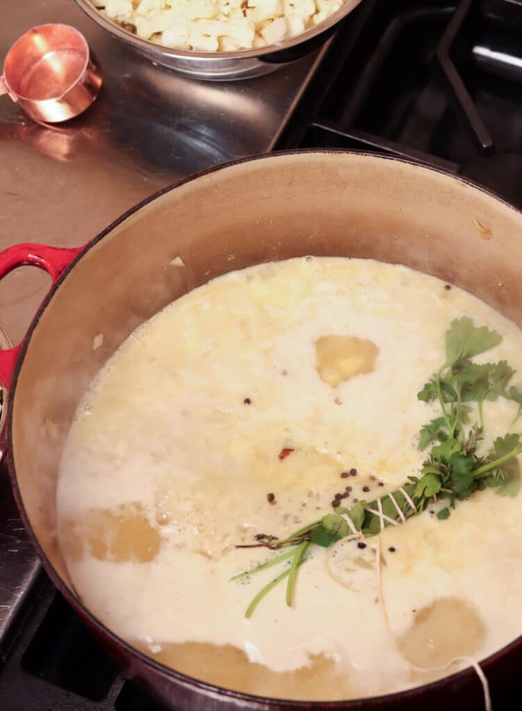 Cauliflower soup with chicken stock, cauliflower, and herb bundle in a large red pot
