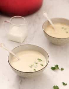 Two bowls of light creamy cauliflower soup with green bits of parsley on top