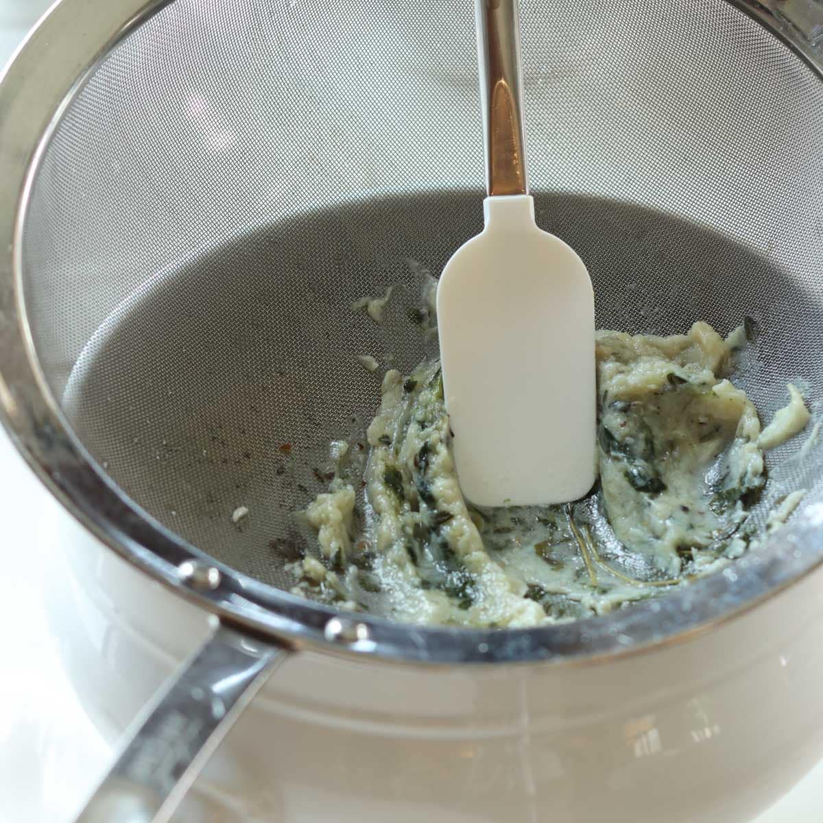 creating a garlic puree by pressing the garlic through the mesh sieve